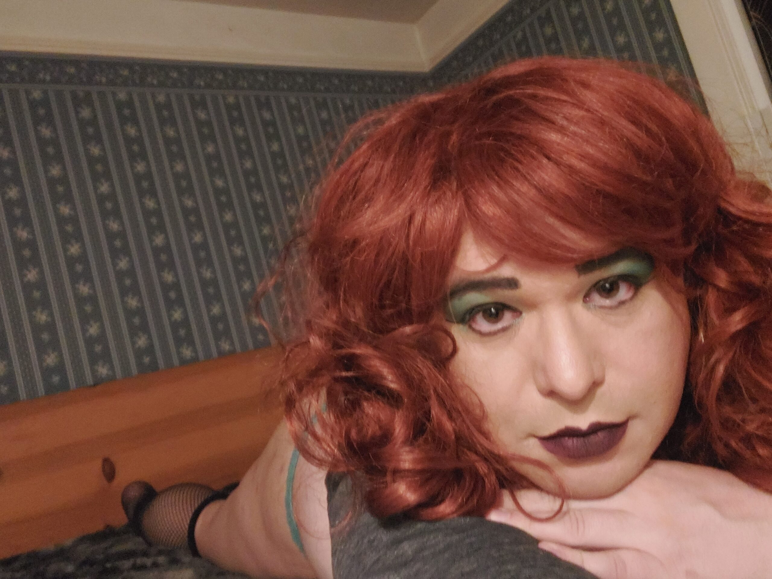 Mistress Ilya is laying on her stomach on her bed looking into the camera. Her hands are crossed under her chin.