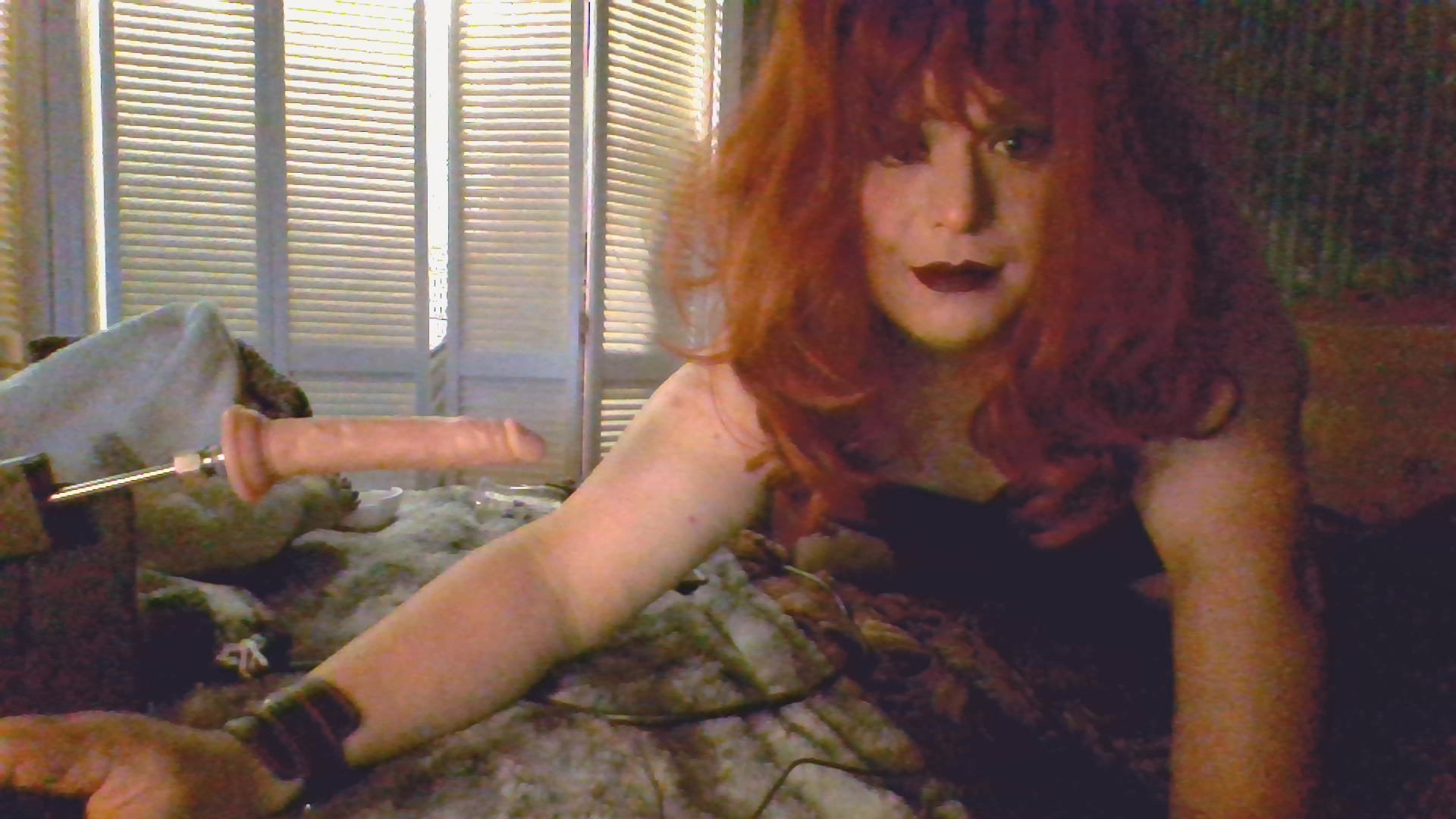 Mistress Ilya is on her bed looking at a camera while her fuck machine is on the bed. 