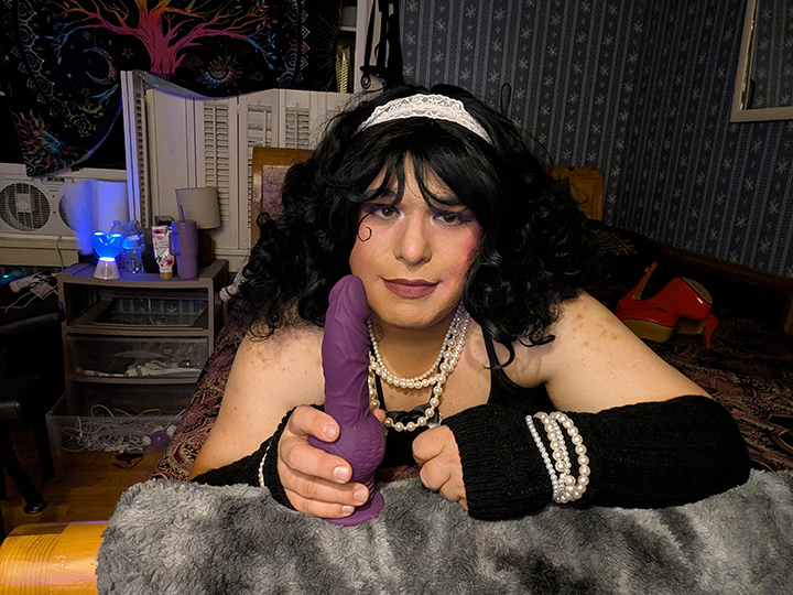 Mistress is holding a dildo while looking at a camera.