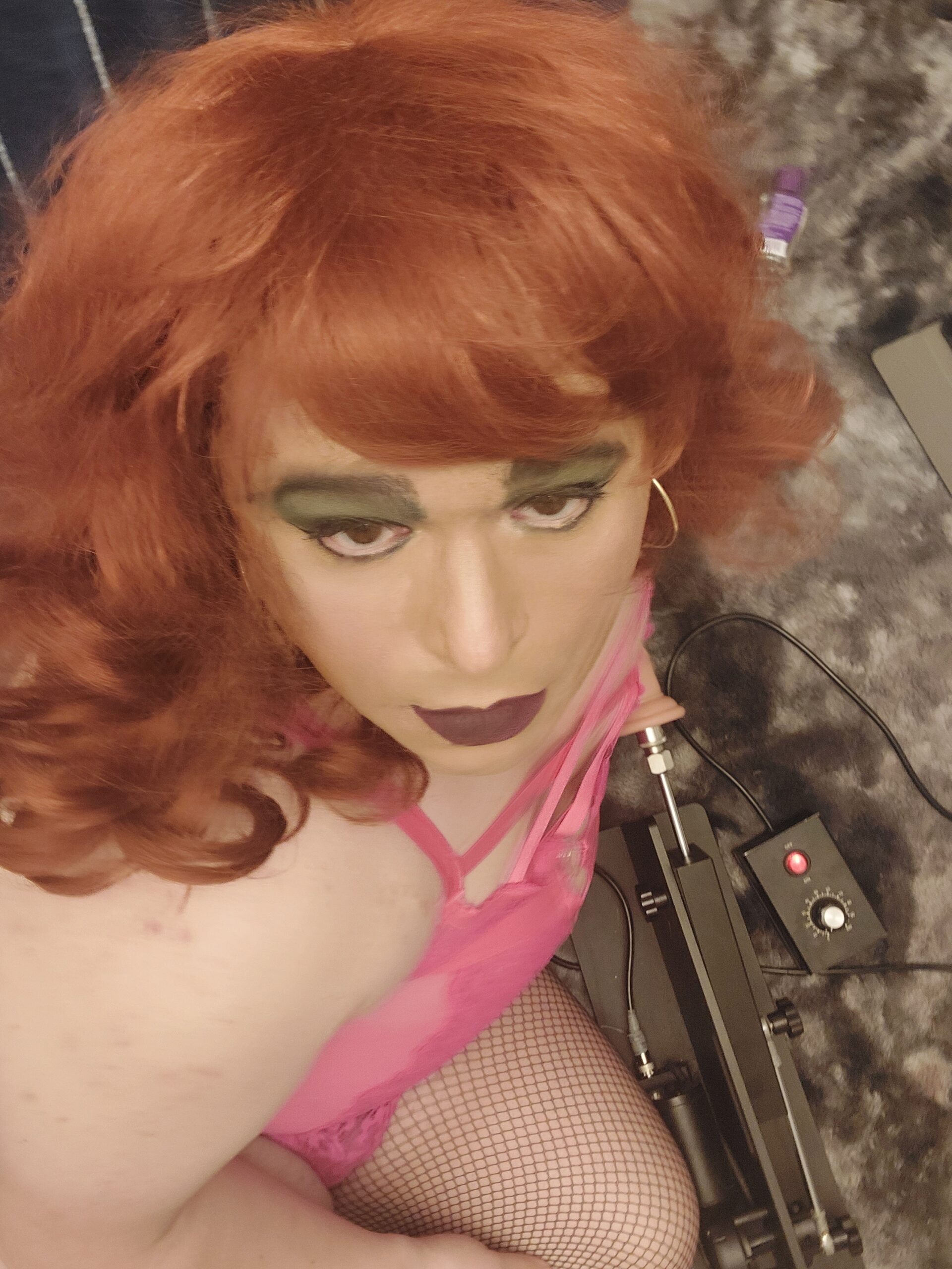 Mistress is looking up at a camera while there is a fuck machine in the background.