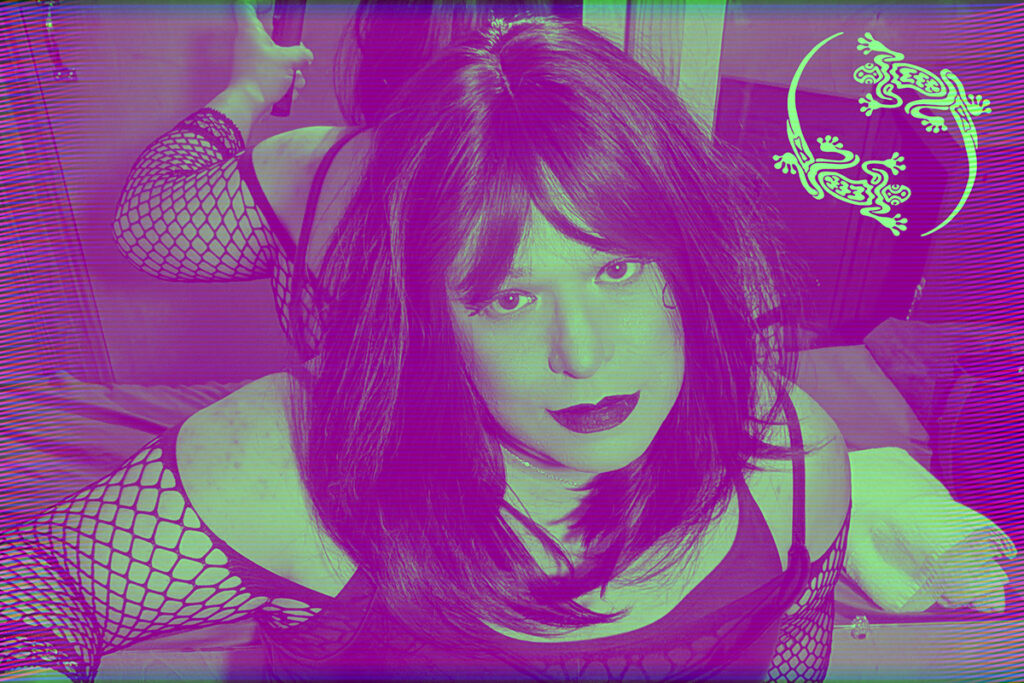 Mistress is kneeling on a bed looking at a camera.