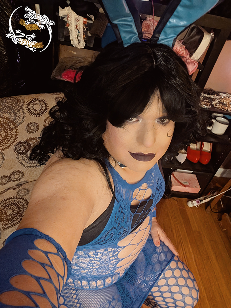 Mistress Ilya is wearing a black bra, a mesh top, and bunny ears while taking a selfie.