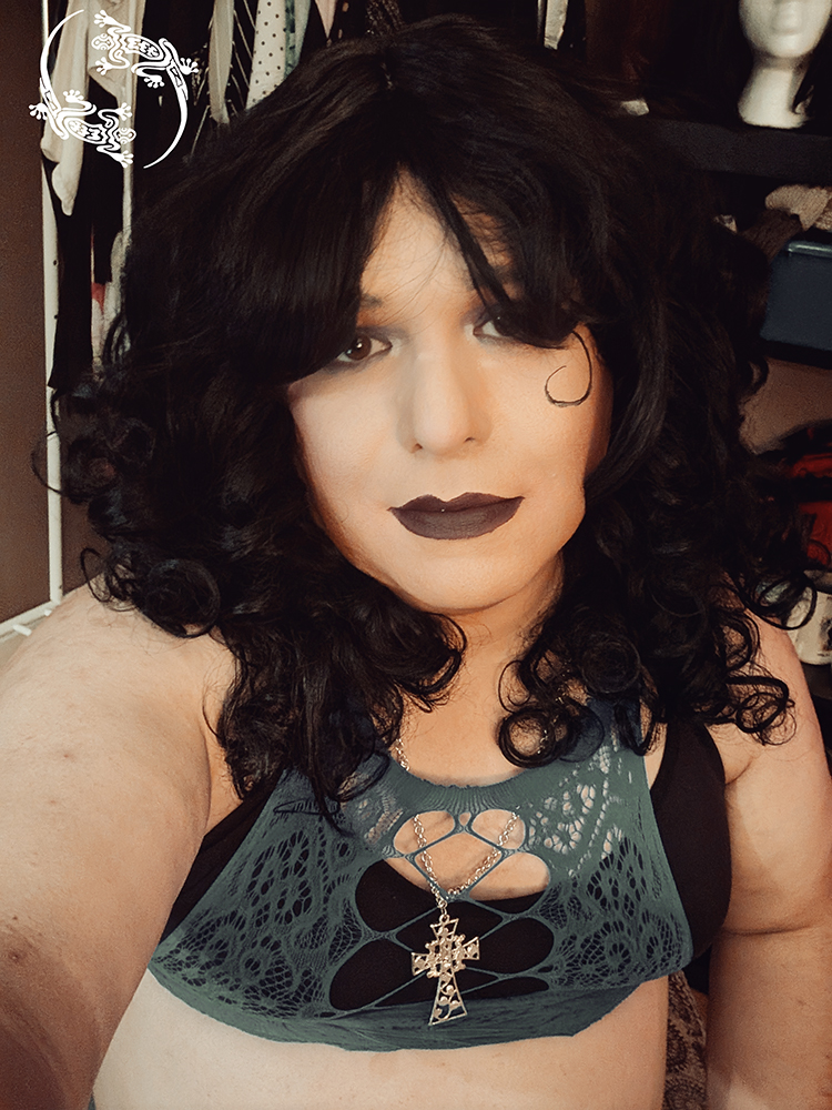 Mistress Ilya is wearing a black bra and a mesh top while taking a selfie.