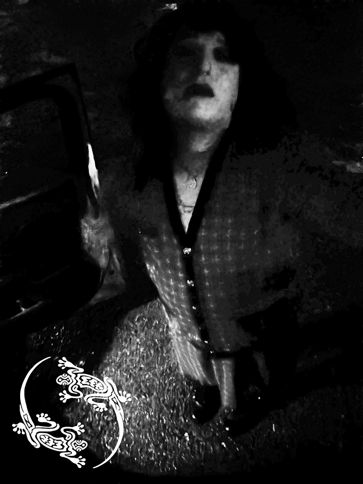Mistress Ilya is standing on a street. There is no color in the photo.