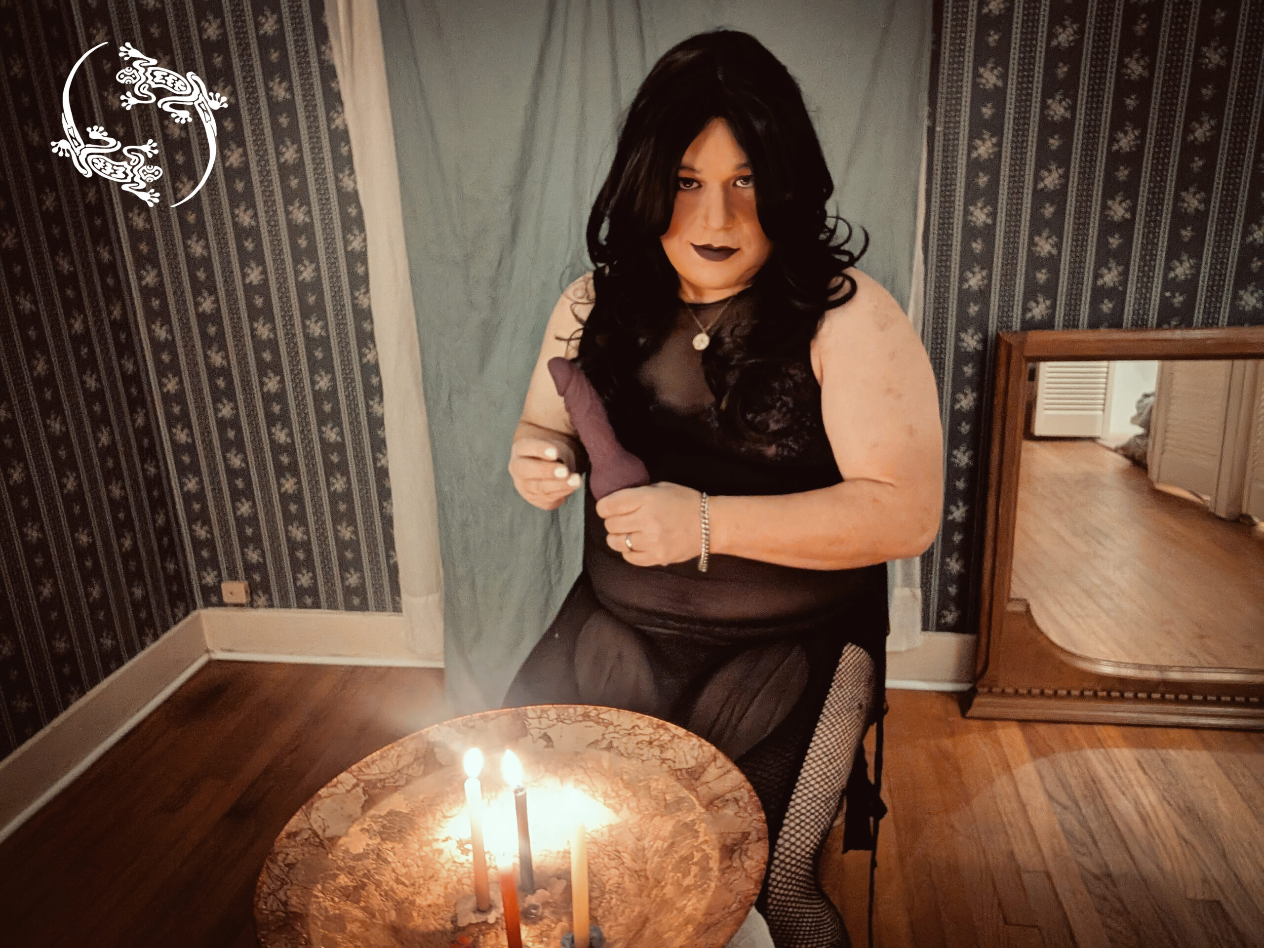 Mistress Ilya is sitting on a chair holding a dildo. Candles are burning.