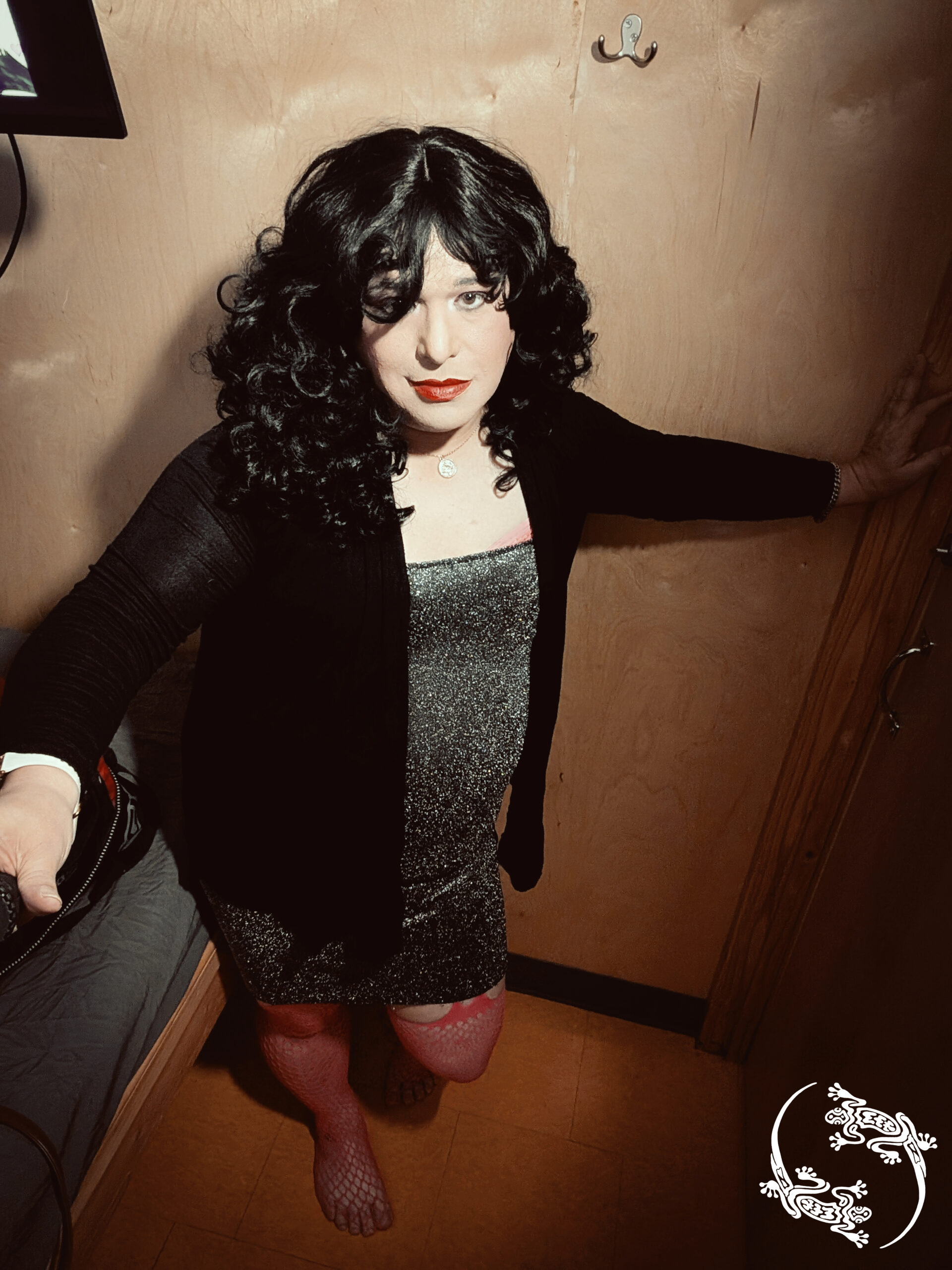 Mistress Ilya is wearing a dress with stockings in a small room.