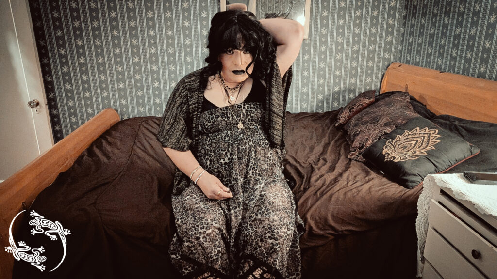 Mistress Ilya is sitting on her bed holding her hair.