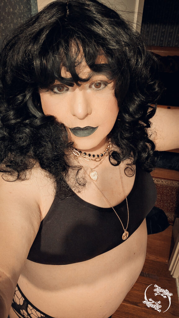 Mistress Ilya is wearing a sports bra and a necklace while looking at the camera. 