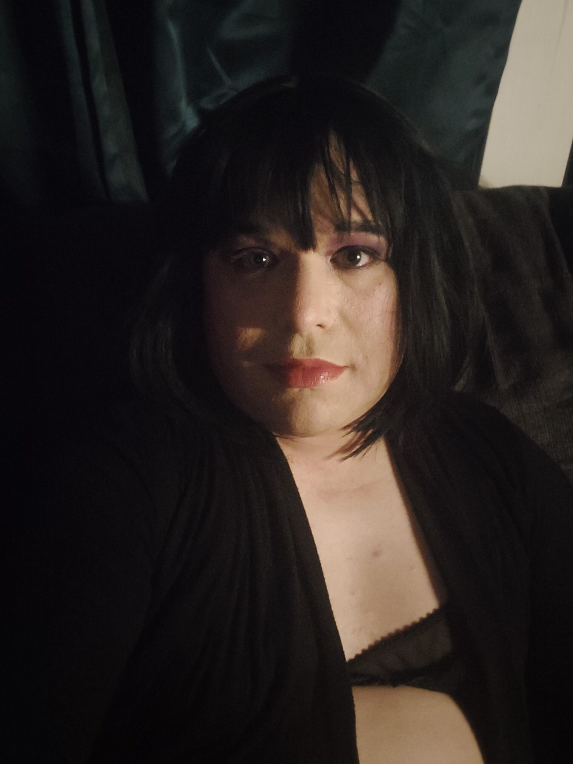 Mistress Ilya is in the dark looking at the camera. 