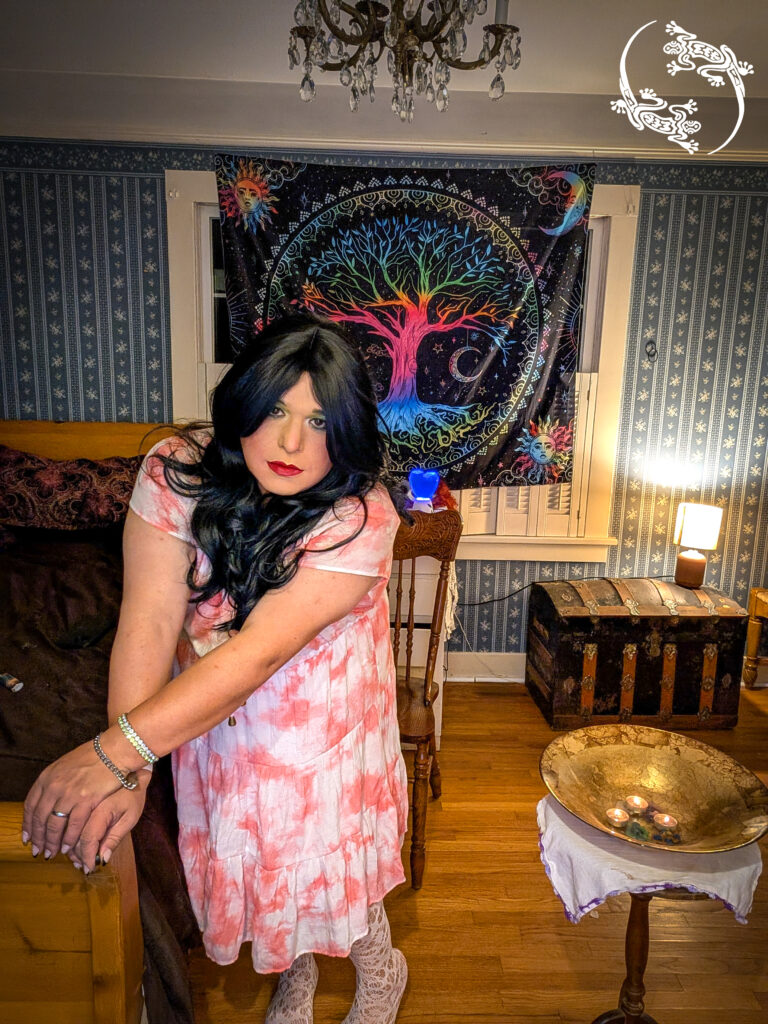 Mistress Ilya is standing by her bed with her altar.