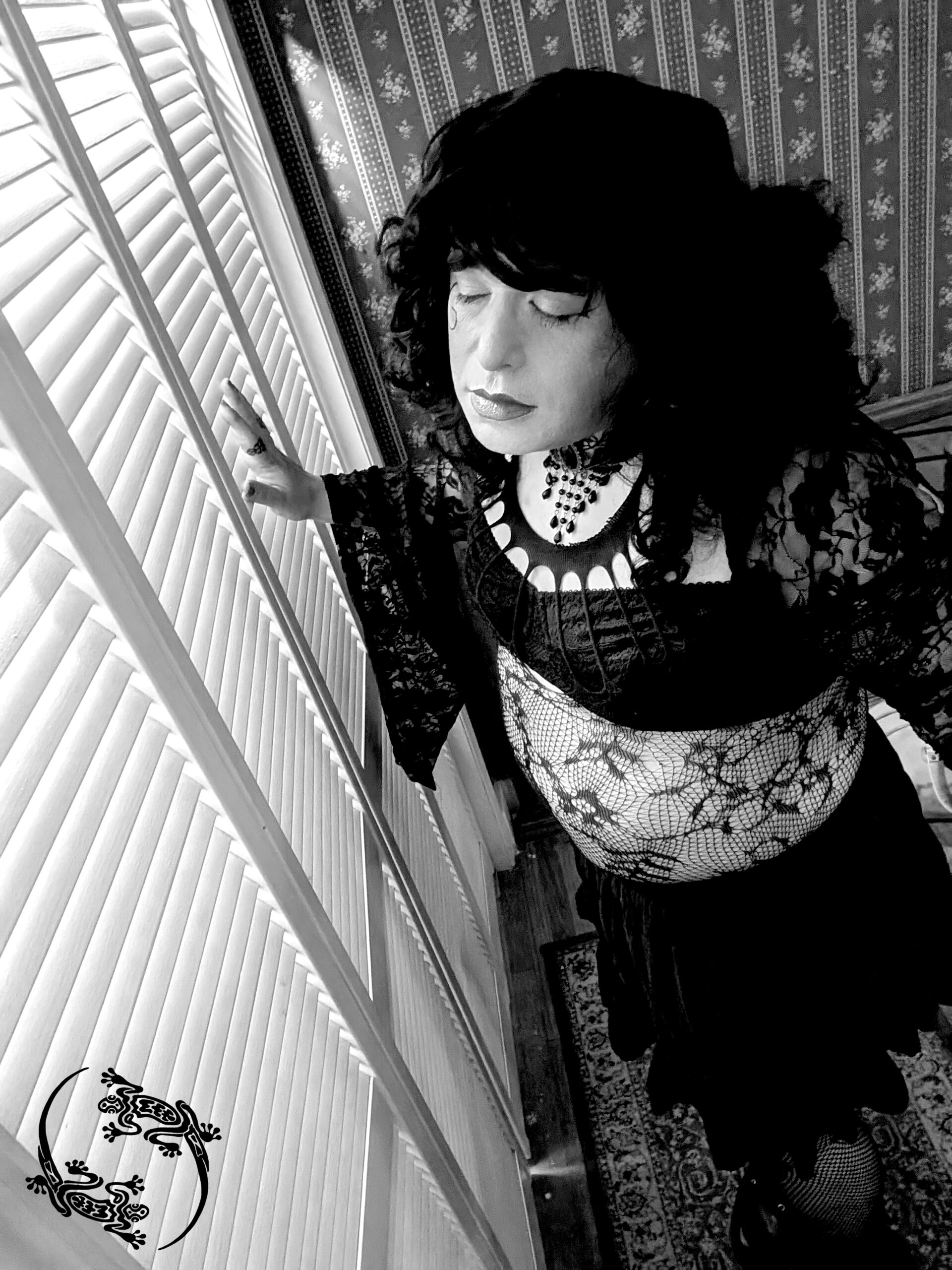 Mistress Ilya is leaning against a closet door that has slats. Her eyes are closed. 
