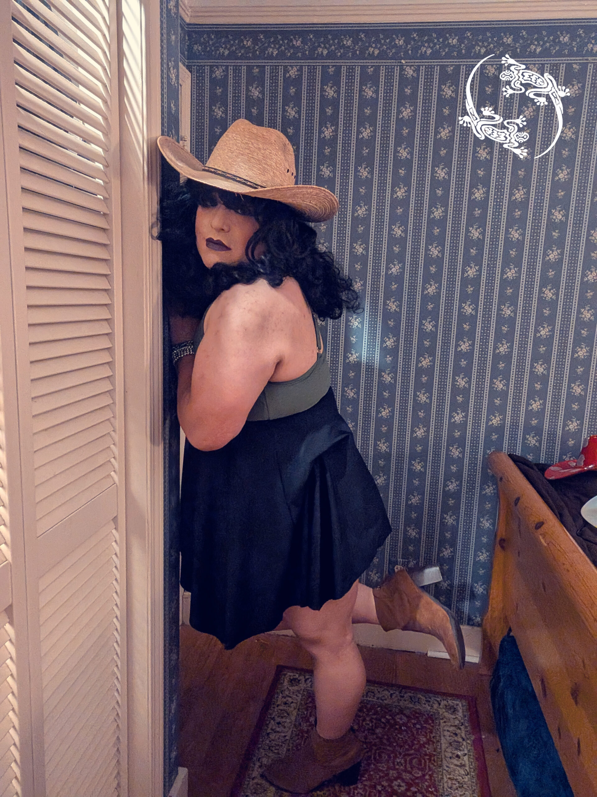 Mistress Ilya is leaning up against a wall. She is wearing a straw hat.