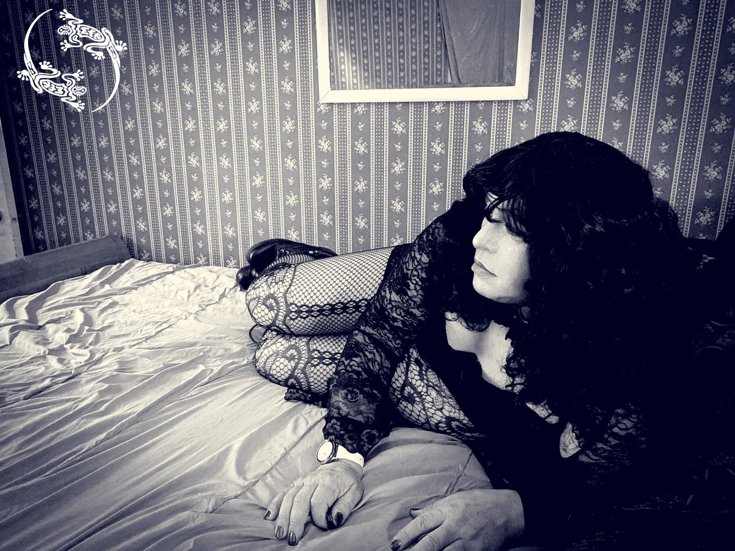 Mistress Ilya is laying on her side on her bed. She is looking away. 