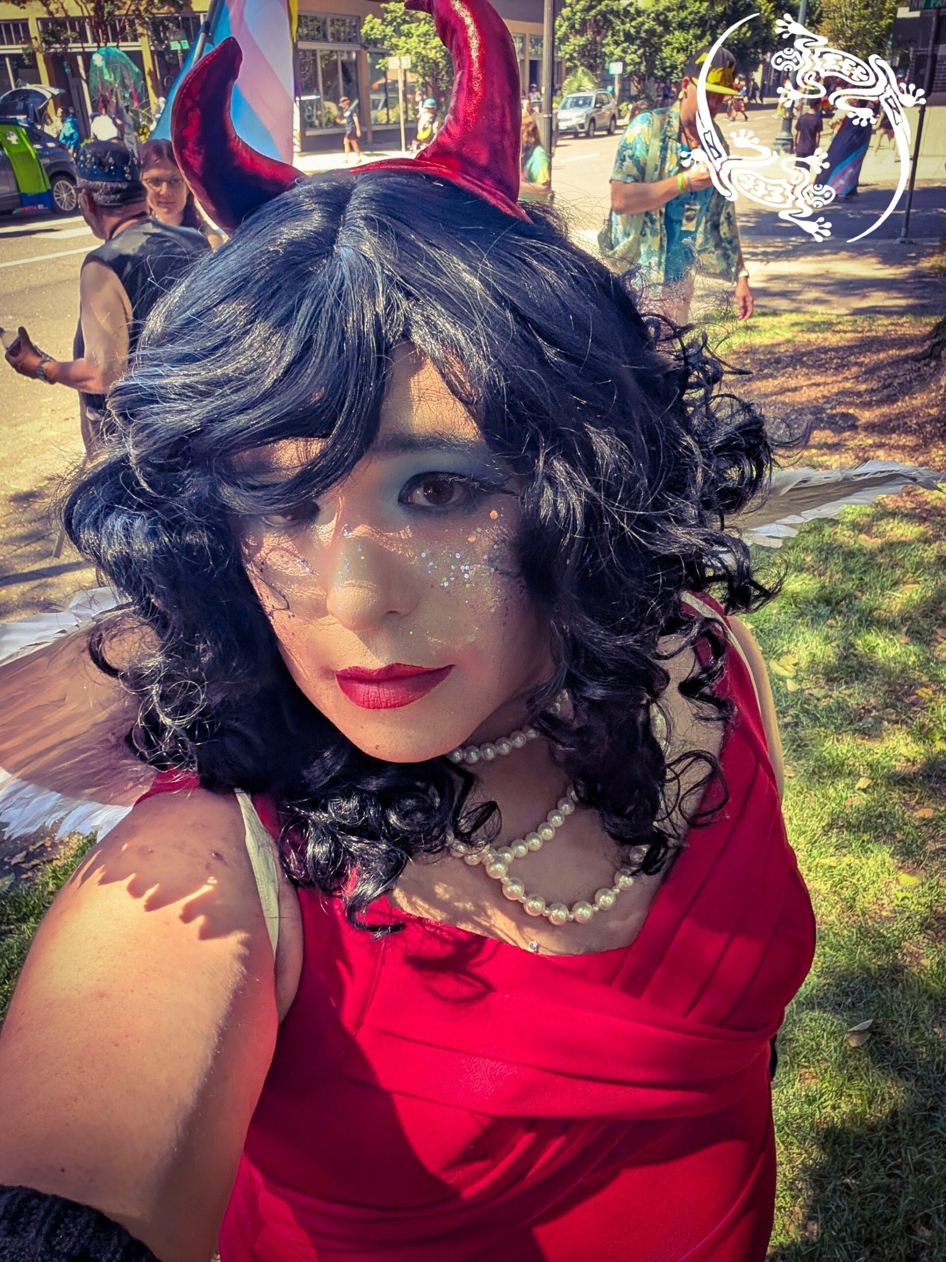 Mistress Ilya is standing in a park taking a selfie. She is wearing plush devil horns.