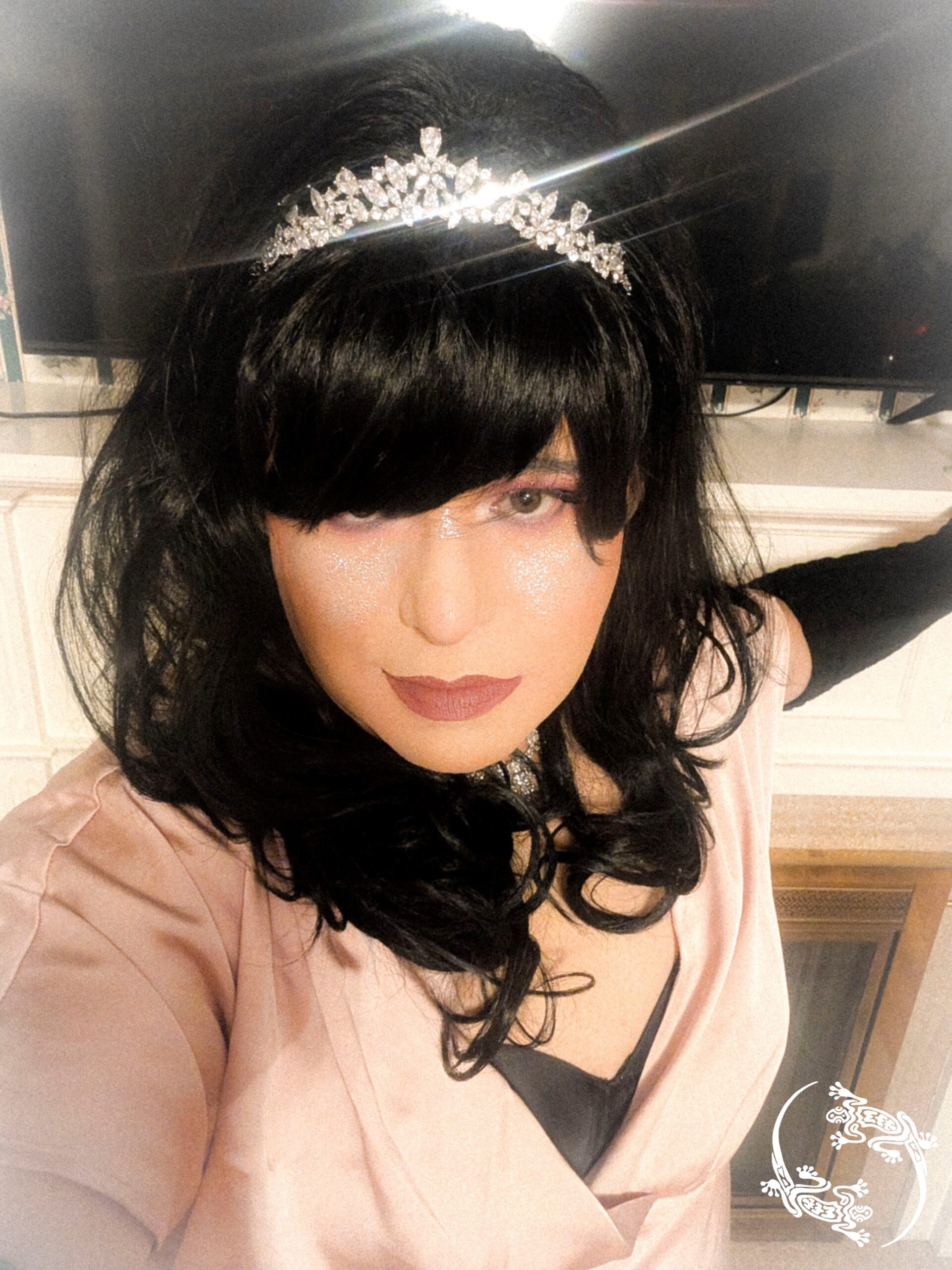 Mistress Ilya is wearing a shiny crown while taking a selfie. 